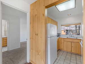 Kitchen with light wood finish cabinetry, freestanding refrigerator, light countertops, and light carpet