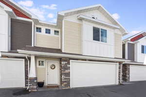 View of front of property featuring board and batten siding, stone siding, a garage, and a shingled roof