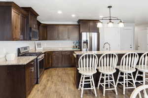 Kitchen featuring stainless steel appliances, dark wood finish cabinets, light stone counters, a breakfast bar, and a kitchen island