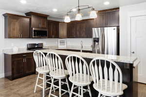 Kitchen with stainless steel appliances, dark wood finish cabinets, a center island, light wood-type flooring, and light stone counters