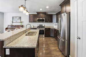 Kitchen with dark wood finish cabinetry, light stone counters, stainless steel appliances, hanging light fixtures, and a textured ceiling
