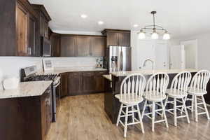 Kitchen with dark wood finish cabinets, stainless steel appliances, a breakfast bar area, light stone countertops, and hanging light fixtures