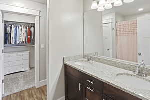 Primary Suite Bathroom with a shower with shower curtain, a walk in closet, double vanity, and light wood-style flooring