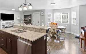 Kitchen featuring dark wood finish cabinets, light stone countertops, a kitchen bar, stainless steel dishwasher, and dark wood finished floors