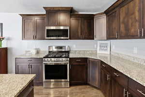 Kitchen featuring stainless steel appliances, dark wood finish cabinets, light stone countertops, and a textured ceiling