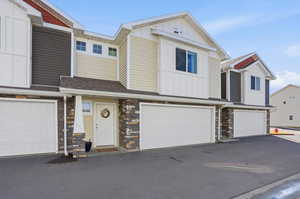 View of front facade featuring stone siding, board and batten siding, roof with shingles, a garage, and driveway