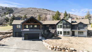View of front of property featuring stone siding, a mountain view, an attached garage, driveway, and a chimney