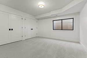 Unfurnished bedroom featuring multiple closets, light carpet, and a textured ceiling