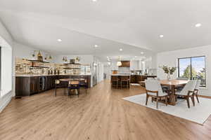 Dining area featuring beverage cooler, light wood-style flooring, lofted ceiling, recessed lighting, and bar area