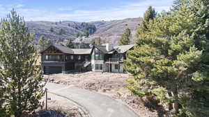 View of front facade featuring stone siding, a mountain view, a balcony, a chimney, and an attached garage