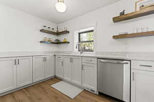 Kitchen with open shelves, stainless steel dishwasher, dark wood-type flooring, light stone countertops, and white cabinets