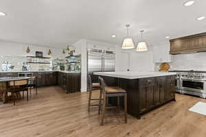 Two tone kitchen featuring dual tone cabinetry, backsplash, a kitchen bar, high end appliances, and a center island