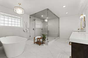 Bathroom with a soaking tub, a shower stall, vanity, light marble finish floors, and a chandelier