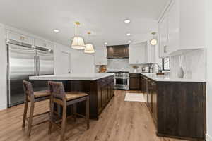 Kitchen featuring two tone cabinetry, a breakfast bar, premium appliances, a center island, and light stone counters