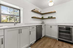 Kitchen with wine cooler, dark wood-style floors, dishwasher, light stone countertops, and open shelves