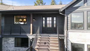 Doorway to property featuring stone siding, roof with shingles, and a porch