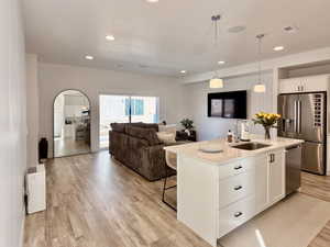 Kitchen featuring white cabinetry, stainless steel appliances, open floor plan, light wood-style flooring, and a kitchen island with sink