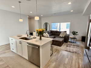 Kitchen featuring white cabinets, stainless steel dishwasher, decorative light fixtures, open floor plan, and light wood-type flooring