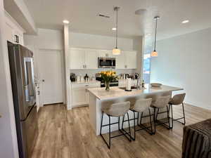 Kitchen featuring stainless steel appliances, a breakfast bar area, hanging light fixtures, a center island with sink, and light wood-type flooring
