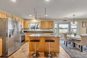 Kitchen featuring stainless steel appliances, a kitchen island, a kitchen breakfast bar, light tile patterned floors, and dark stone counters