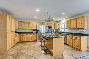 Kitchen featuring a breakfast bar, stainless steel appliances, dark stone counters, recessed lighting, and an island with sink