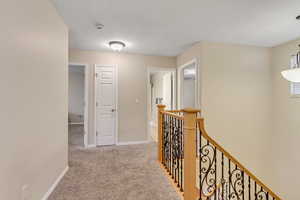 Hallway with an upstairs landing and light colored carpet