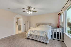 Primary bedroom featuring light carpet, connected bathroom, arched walkways, and ceiling fan