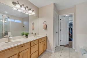 Full bathroom with a garden tub, double vanity, a stall shower, a walk in closet, and light tile patterned floors