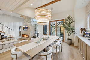 Dining space with light wood-style floors, a stone fireplace, a chandelier, and beam ceiling