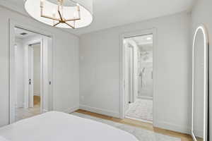 Bedroom with hanging lights, light wood-type flooring, and ensuite bath