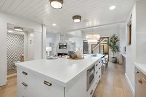 Kitchen featuring white cabinetry, a fireplace, a kitchen island, light wood-type flooring, and stainless steel microwave