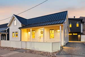 View of front facade featuring covered porch, a standing seam roof, decorative driveway, a gate, and a garage