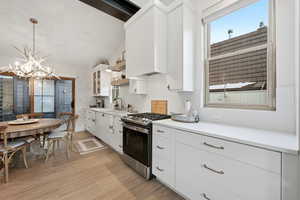 Kitchen with white cabinetry, stainless steel range with gas stovetop, light wood finished floors, hanging lights, and healthy amount of natural light