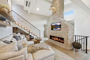 Living area featuring a high ceiling, light wood-style flooring, and a stone fireplace