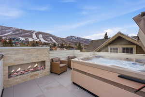 View of patio / terrace with a mountain view, an outdoor stone fireplace, and a hot tub