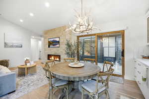 Dining space featuring light wood-style flooring, lofted ceiling, a stone fireplace, and suspended lighting