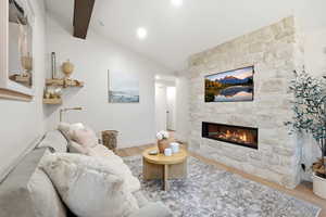 Living room with light wood-style flooring, a fireplace, and vaulted ceiling with beams