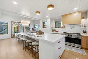 Dual tone kitchen featuring high end stainless steel range oven, a breakfast bar, extractor fan, light wood finished floors, and wood ceiling