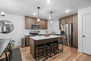 Kitchen featuring stainless steel appliances, a breakfast bar area, light wood finished floors, a kitchen island, and hanging light fixtures