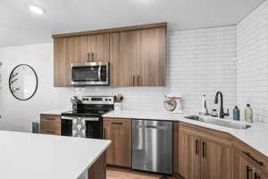 Kitchen featuring stainless steel appliances, wood finish cabinets, light stone countertops, decorative backsplash, and modern cabinets