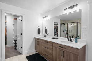 Full bath featuring a walk in closet, a stall shower, double vanity, a textured ceiling, and light tile patterned floors