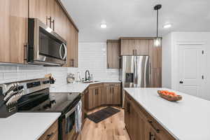 Kitchen featuring stainless steel appliances, light wood-style floors, wood finish cabinetry, and pendant lighting
