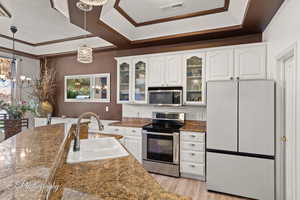 Kitchen featuring stainless steel appliances, white cabinets, glass fronted cabinets, dark stone counters, and hanging lights