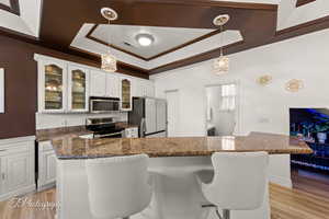Kitchen featuring glass fronted cabinets, white cabinetry, hanging light fixtures, stainless steel appliances, and a tray ceiling