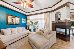 Living room featuring wood finished floors, ceiling fan, a multi sided fireplace, and ornamental molding