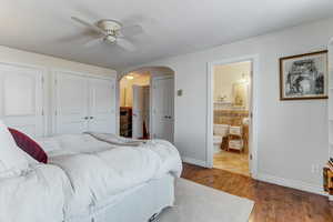 Bedroom with wood-type flooring, arched walkways, ceiling fan, and ensuite bathroom