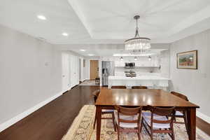 Dining room with dark wood-style floors, a chandelier, and a raised ceiling