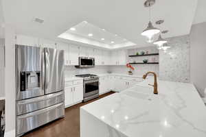 Kitchen featuring stainless steel appliances, white cabinets, a peninsula, light stone counters, and pendant lighting