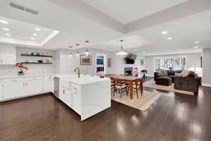 Kitchen with a peninsula, white cabinetry, open floor plan, light stone counters, and a raised ceiling