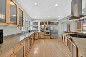 Kitchen with glass insert cabinets, stainless steel appliances, light stone counters, recessed lighting, and island range hood